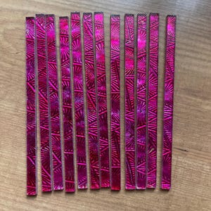 May include: A collection of pink, rectangular mosaic tiles with a textured, starburst-like pattern. The tiles are arranged on a wooden surface, showcasing their vibrant color and design. These tiles could be used for various craft projects.