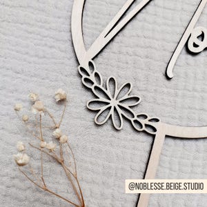 Pode incluir: Corte de madeira da letra "A" com um design floral ao redor da borda. A letra tem a forma de um c&iacute;rculo e o design floral inclui folhas e uma flor grande.