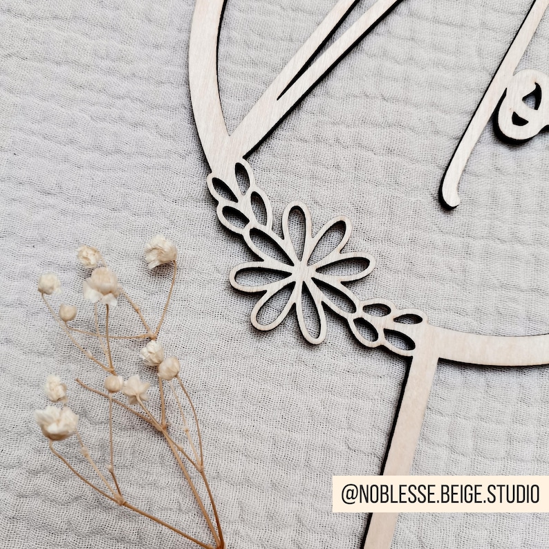 Pode incluir: Corte de madeira da letra "A" com um design floral ao redor da borda. A letra tem a forma de um c&iacute;rculo e o design floral inclui folhas e uma flor grande.
