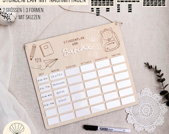 Puede incluir: Un tablero de horario escolar de madera con una cuadrícula de rectángulos en blanco para cada día de la semana. El tablero tiene una ilustración de lápiz, cuaderno y avión de papel. El texto en el tablero incluye "STUNDENPLAN" y "Sarina Beige". Se incluye un marcador negro.