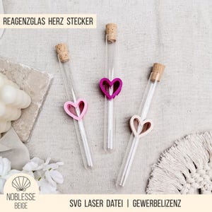 May include: Three clear glass test tubes with cork stoppers, each adorned with a heart-shaped decoration in pink, fuchsia, and light beige. The text "REAGENZGLAS HERZ STECKER" is at the top. The text "SVG LASER DATEI | GEWERBELIZENZ" is at the bottom.