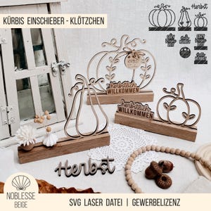 May include: Wooden fall-themed decorations featuring pumpkin and pear shapes. The decorations include the word "Herbst" and "herbstlich WILLKOMMEN". The items are displayed on a white surface with a window in the background.