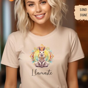 Op de afbeelding: Een beige t-shirt met een kleurrijk mandala-ontwerp met een lama in een meditatieve houding. De tekst "llamaste" is onder de mandala gedrukt.