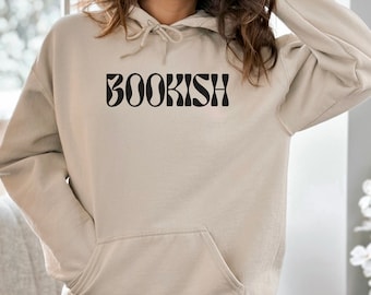 May include: A beige hoodie with a front pocket and drawstring hood. The word "BOOKISH" is printed across the chest in a black, retro-style font. The hoodie is made of a soft material.