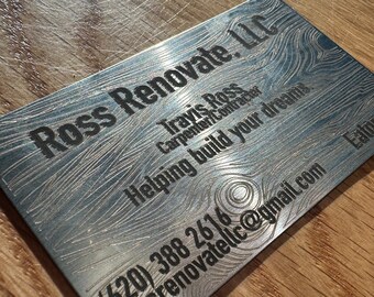 May include: A silver business card with the text "Ross Renovate, LLC" and the contact information for Travis Ross, Carpenter/Contractor. The card also includes the text "Helping build your dreams." and the phone number (620) 388 2616. The email address is rossrenovatellc@gmail.com and the location is Eaton, CO.