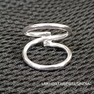 Puede incluir: Anillo de nariz de plata de doble aro con una pequeña piedra preciosa transparente. El anillo está hecho de dos aros entrelazados.