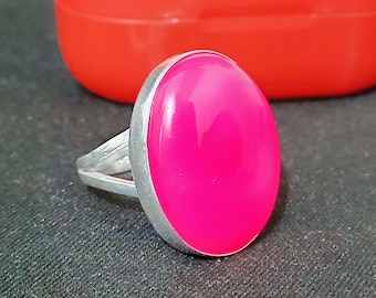 May include: A silver ring with a large, oval-shaped, bright pink gemstone. The ring is set in a simple, silver band.