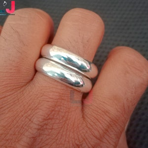 May include: Two silver rings stacked on a finger. The rings are smooth and shiny.