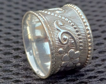 Könnte beinhalten: Ein silberner Ring mit einem floralen Design. Der Ring ist breit und hat eine strukturierte Oberfläche. Das Design ist filigran und detailliert.