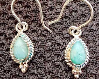 May include: A pair of silver dangle earrings with a teardrop-shaped light green stone set in a silver bezel. The earrings have a twisted wire design and a small silver bead detail at the bottom.