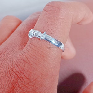 Può includere: Un anello d'argento con un design attorcigliato. L'anello è indossato su un dito.