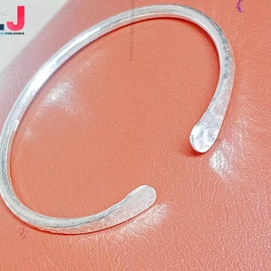 May include: A silver bangle bracelet with a hammered finish. The bracelet is open and has a slightly curved shape.
