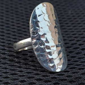 Peut inclure: Une bague en argent martelée avec une large bande de forme ovale. La bague a une finition martelée texturée.