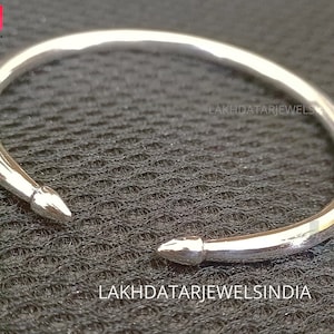 May include: A silver bangle bracelet with pointed ends. The bracelet is simple and sleek, with a smooth, polished finish.