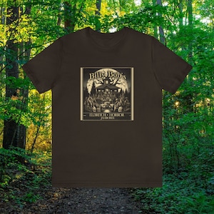 Puede incluir: Una camiseta marrón con un estampado gráfico de una casa espeluznante con el texto "Billy Bob's Eldritch Horror Jamboree".