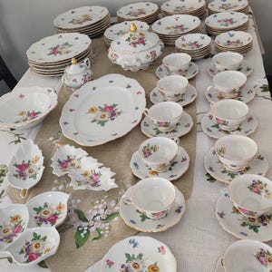 May include: A complete vintage porcelain tea set with floral designs. The set includes plates, saucers, teacups, a sugar bowl, a serving dish, and a covered serving bowl. The floral pattern features pink, yellow, and blue flowers with gold trim.