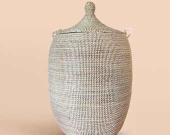 May include: A large, oval-shaped, woven storage basket with a lid. The basket is made of natural materials and has a light brown color. The lid has a small knob on top.