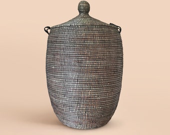 May include: A black and white woven storage basket with a lid and handles. The basket is made of natural materials and has a traditional design.