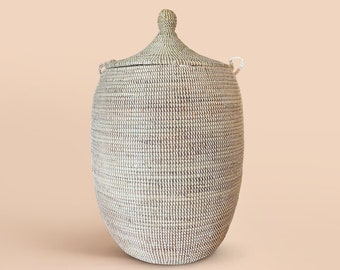 May include: A large, white woven basket with a lid and handles. The basket is made of natural materials and has a traditional design.