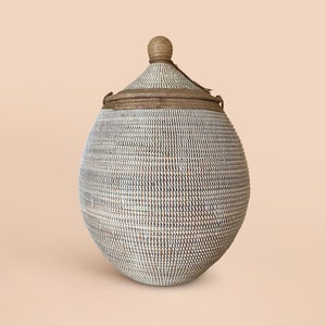 May include: A white and brown woven basket with a lid and a wooden knob. The basket is round and has a natural, rustic look.