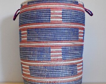 May include: A blue and pink woven storage basket with a lid. The basket has a geometric pattern and is made of natural materials.