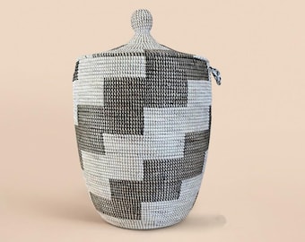 May include: A large, white and black woven storage basket with a lid. The basket has a geometric pattern and a knob on the lid.