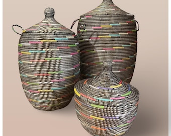 May include: Three black woven storage baskets with colorful stripes. The baskets are of different sizes and have lids.