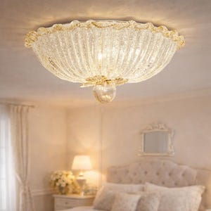 Pode incluir: Uma luminária de teto de vidro transparente com acabamento dourado e um design texturizado e canelado. A luz tem uma base em forma de flor e é montada em um teto branco. A luminária está em um quarto.
