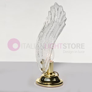 Può includere: Una lampada da tavolo in vetro trasparente con un design ondulato e testurizzato. La lampada ha una base dorata e una singola lampadina.