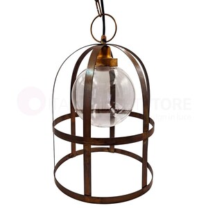 May include: A hanging pendant light with a clear glass globe encased in a cage-like frame. The frame is made of a dark, rusty-brown metal, and the fixture has a brass-colored top. The light hangs from a black cord.