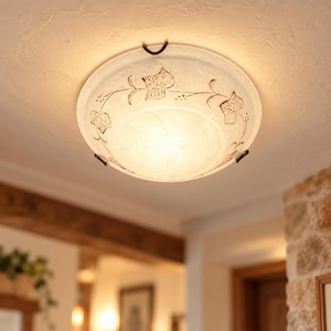 Pode incluir: Uma luminária de teto redonda de vidro fosco com um padrão decorativo de videiras e folhas marrons na borda. A luz é fixada ao teto com três clipes de metal escuro, emitindo um brilho quente e suave.