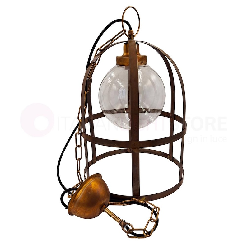 May include: A vintage-style pendant light fixture. It features a clear glass globe encased in a rusty brown metal cage. The fixture includes a chain, a black wire, and a decorative brass-colored canopy. The design evokes an industrial aesthetic.
