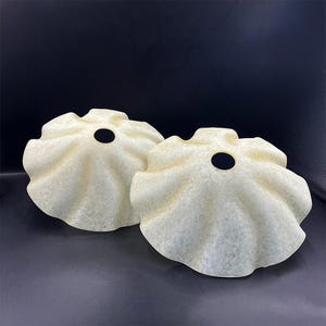 Op de afbeelding: Twee gebroken witte, gerimpelde lampenkappen met een gat in het midden voor een lamp.