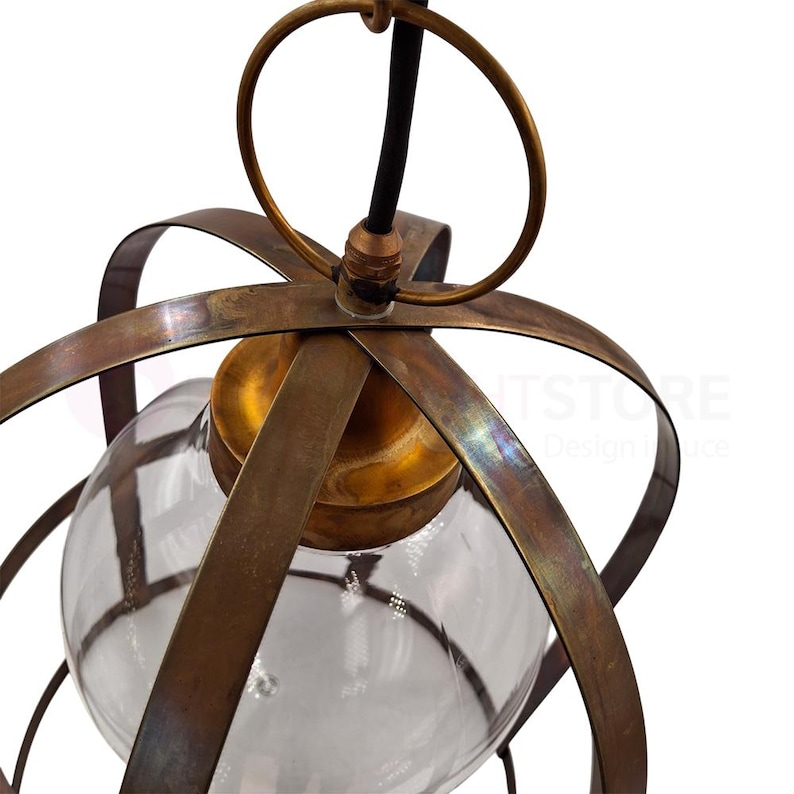 May include: A vintage-style pendant light fixture with a clear glass globe encased in a bronze-colored metal frame. The fixture has a circular top ring and a black cord. The metal has a distressed finish.
