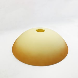 Può includere: Un paralume per lampada rotondo in vetro con un top giallo chiaro e un fondo arancione scuro.