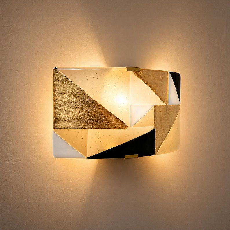 K&ouml;nnte beinhalten: Geometrische Wandleuchte mit goldenem, schwarzem, wei&szlig;em und beigem Design. Die Leuchte hat eine rechteckige Form mit gew&ouml;lbter Front und wird von innen beleuchtet, wodurch ein warmes Licht entsteht.