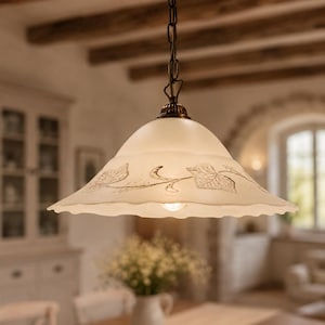 Może przedstawiać: Lampa wisząca z matowego szkła z falistą krawędzią i delikatnym wzorem brązowych, wytrawianych liści bluszczu. Lampa zawieszona jest na ciemnym metalowym łańcuchu i posiada mosiężną nasadkę na szczycie klosza w kształcie kopuły.