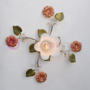 K&ouml;nnte beinhalten: Eine wei&szlig;e Deckenleuchte mit floralem Design. Die Leuchte hat f&uuml;nf Bl&uuml;ten, von denen vier pfirsichfarben und eine wei&szlig; sind. Die wei&szlig;e Bl&uuml;te hat eine Gl&uuml;hbirne in der Mitte. Die Bl&uuml;ten sind an einem Metallst&auml;ngel mit gr&uuml;nen Bl&auml;ttern befestigt.