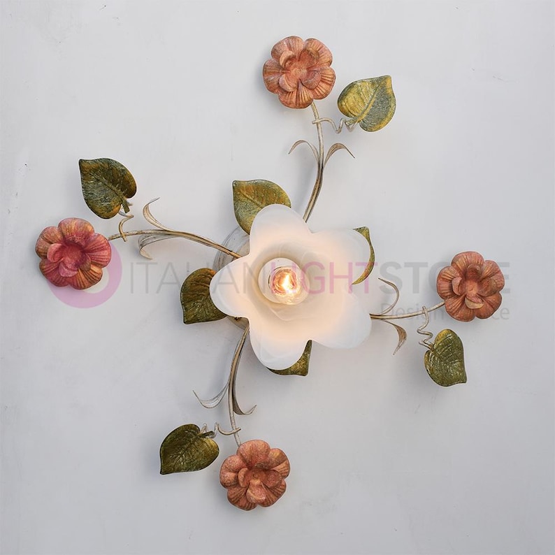 K&ouml;nnte beinhalten: Eine wei&szlig;e Deckenleuchte mit floralem Design. Die Leuchte hat f&uuml;nf Bl&uuml;ten, von denen vier pfirsichfarben und eine wei&szlig; sind. Die wei&szlig;e Bl&uuml;te hat eine Gl&uuml;hbirne in der Mitte. Die Bl&uuml;ten sind an einem Metallst&auml;ngel mit gr&uuml;nen Bl&auml;ttern befestigt.