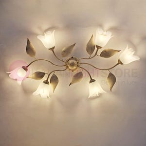 Può includere: Un lampadario a soffitto a tema floreale con finitura bronzo. L'apparecchio presenta più paralumi in vetro bianco a forma di tulipano e accenti di foglie color bronzo. La luce è progettata per essere montata a soffitto.