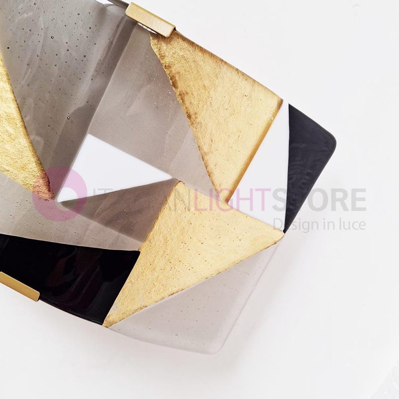 K&ouml;nnte beinhalten: Geometrische dekorative Schale mit goldenen, schwarzen, wei&szlig;en und grauen Dreiecksabschnitten. Die Schale hat ein modernes Design mit gl&auml;nzendem Finish und goldfarbenen Metallakzenten. Es ist ein dekorativer Artikel.