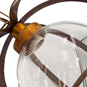 May include: Close-up of a decorative light fixture featuring a clear glass globe encased in a bronze-colored metal frame. The fixture has a vintage aesthetic, with a brass-colored socket and a series of curved metal elements extending outward from the globe.