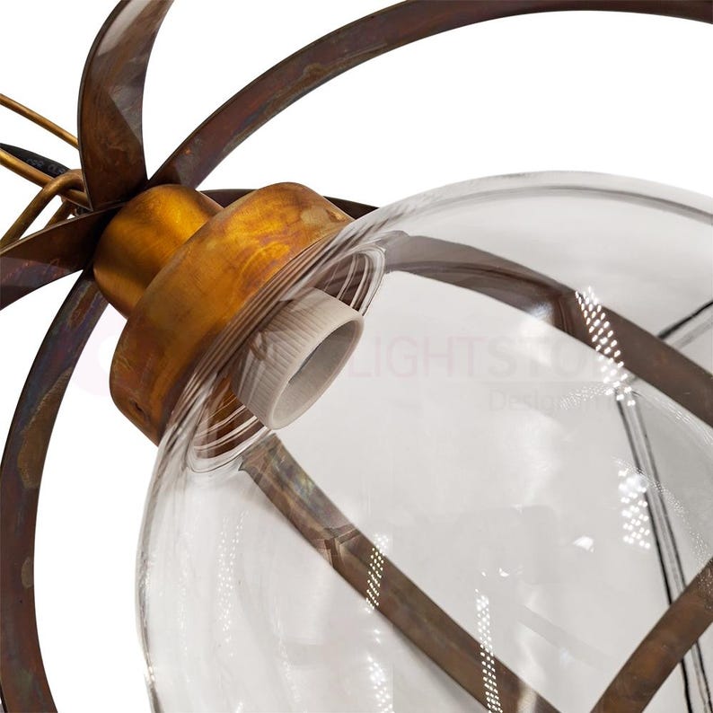 May include: Close-up of a decorative light fixture featuring a clear glass globe encased in a bronze-colored metal frame. The fixture has a vintage aesthetic, with a brass-colored socket and a series of curved metal elements extending outward from the globe.