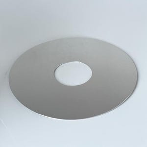 Peut inclure: Un objet métallique circulaire argenté avec un trou central. L'objet est posé sur un fond blanc, et l'éclairage crée des reflets et des ombres subtils sur sa surface. Le design est simple et moderne.
