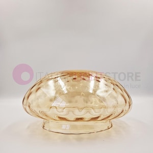 Może przedstawiać: Klosz lampy wykonany z jasnego bursztynowego szkła z falistym, fakturowanym wzorem. Klosz ma zaokrąglony wierzchołek i płaską podstawę.