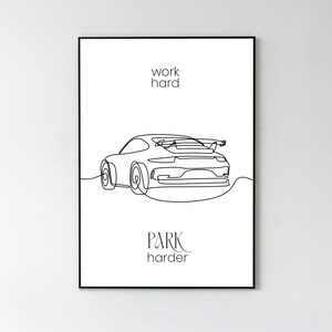 Op de afbeelding: Zwart ingelijste kunstdruk met een minimalistische lijntekening van een sportwagen. De woorden "work hard" staan boven de auto en "park harder" eronder. Het kunstwerk staat op een witte achtergrond.