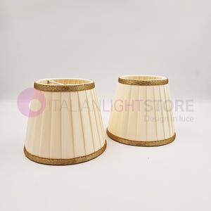 Può includere: Due paralumi plissettati color avorio con bordino dorato. I paralumi sono in tessuto e hanno un design classico.