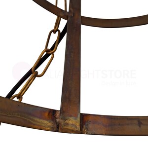 May include: Close-up of a section of a rustic, metal chandelier. The frame is a dark, aged bronze color with visible weld marks. A gold-colored chain and a black wire are attached to the frame. The text "ITALIA LIGHTSTORE" is partially visible.