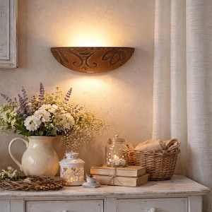 Op de afbeelding: Een warme, uitnodigende interieurscène met een decoratieve wandlamp. Een boeket witte en paarse bloemen staat in een crèmekleurige kan. Een kleine witte lantaarn, boeken en een rieten mand dragen bij aan de sfeer.