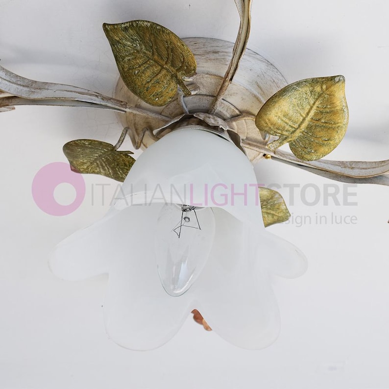 K&ouml;nnte beinhalten: Eine wei&szlig;e Deckenleuchte mit floralem Design. Die Leuchte hat f&uuml;nf Arme mit Bl&auml;ttern und einen wei&szlig;en Glasschirm in Form einer Blume.